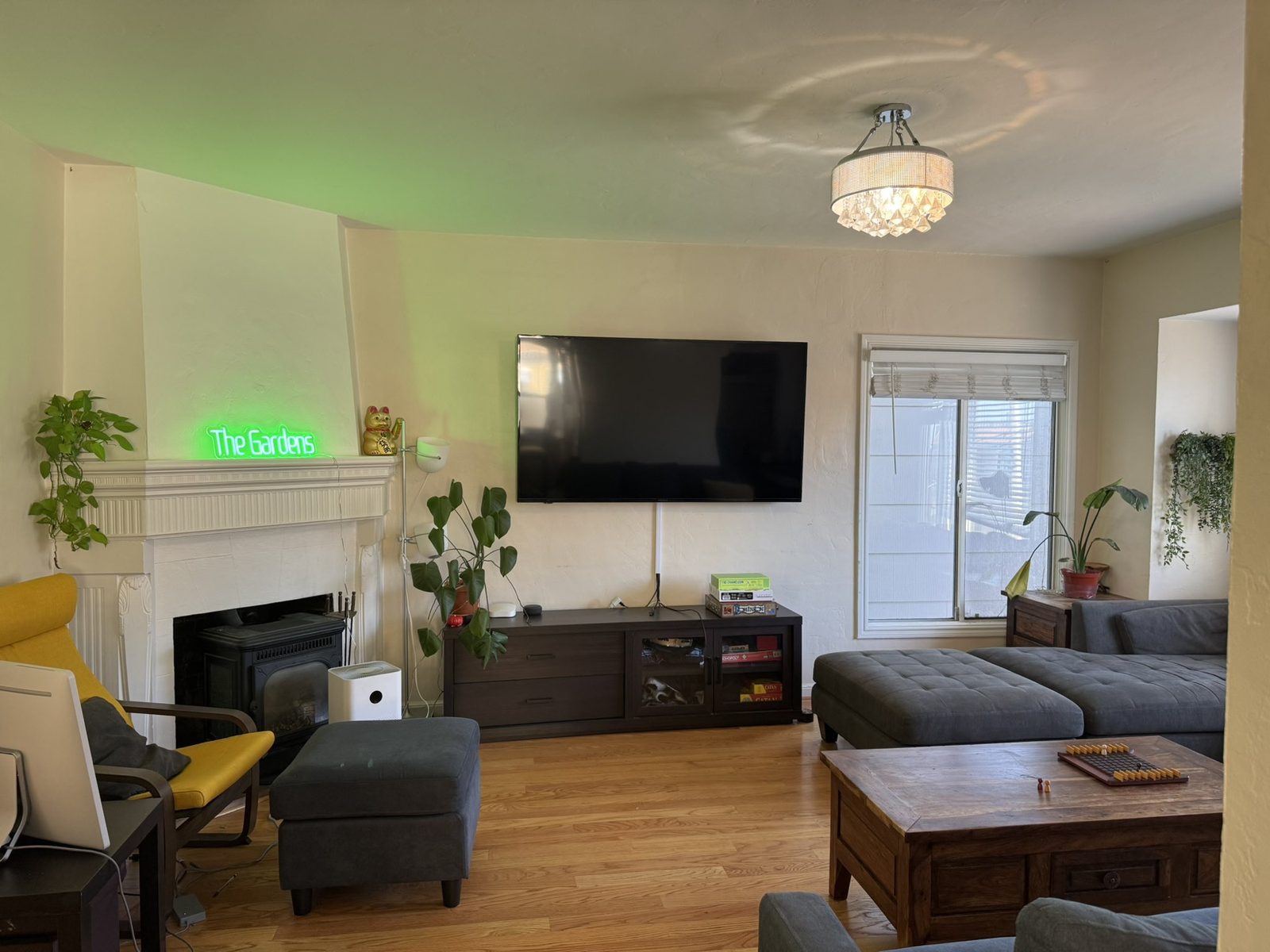The living room lit green by a neon sign reading The Gardens above the fireplace.